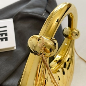 Détail d'un sac de soirée doré avec poignée à nœud sphérique unique et finition métal brillant