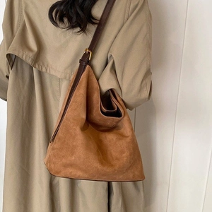 Brown suede tote bag with leather straps and gold buckle worn with a trench coat