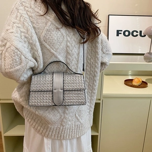 Detail of silver woven texture handbag with magnetic clasp on beige sweater background