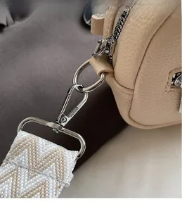 Detail of silver metal hook and woven wide strap on beige pebbled leather bag