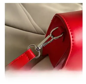 Detailed close-up of the silver metal hook and red leather strap connection of the bag