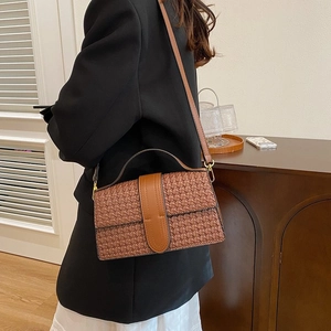 Detail of caramel woven shoulder bag with leather strap shown on a female model