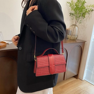 Detail of red woven texture handbag with golden hardware and leather strap in home setting