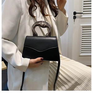 Detail of minimalist black leather handbag with a silver artistic metal handle on a model