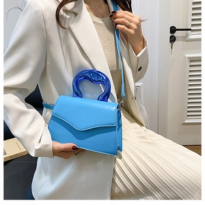Detail of blue crossbody bag with unique translucent acrylic handle and matte leather finish