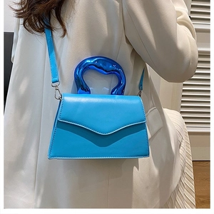 Detail of blue envelope handbag with artistic wave metal handle and matte leather finish