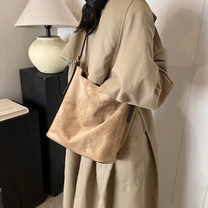 Detail of khaki suede bucket bag with slim brown leather strap shown on model in studio