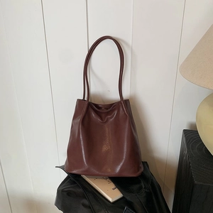 Detailed view of deep brown faux leather tote bag on black leather jacket with magazines