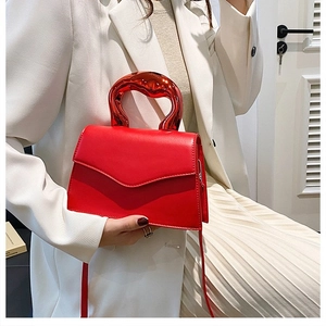 Close-up of vibrant red crossbody bag with sculptural metallic handle on white blazer
