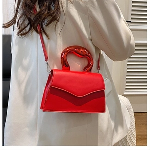 Detail of red crossbody bag with unique fluid-shaped metal handle on white suit
