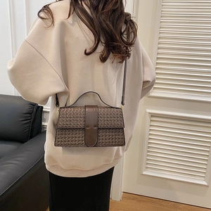 Detail of a dark brown woven textured crossbody bag with metal buckle and top handle