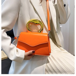 Close-up of bright orange crossbody bag featuring a thick gold metallic handle and flap