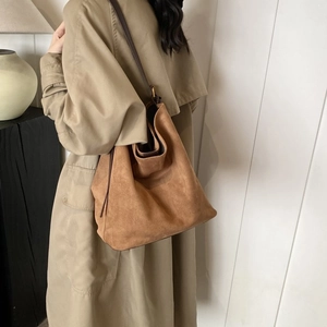 Hobo style camel suede tote bag with slim brown shoulder straps on a beige coat