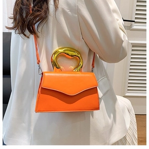 Detail of bright orange crossbody bag featuring a designer fluid gold metallic handle