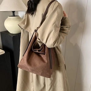 Detail view of brown matte suede bucket bag with long leather strap on beige trench coat