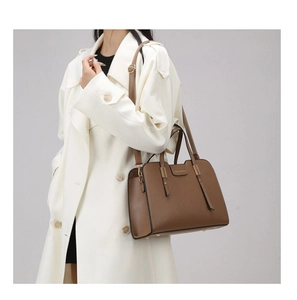 Detail of a brown textured faux leather handbag with gold hardware on a white wool coat