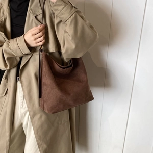 Detail of a brown matte suede shoulder bag with thin straps on a beige trench coat