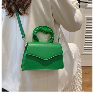 Detail of green leather handbag featuring a unique metallic curved handle and stitching