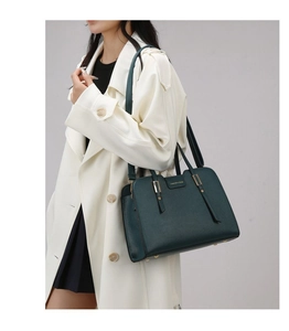 Detail of dark green textured leather handbag with gold buckle and fashion logo