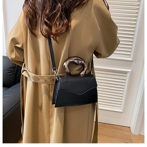 Modern black flap shoulder bag with unique metallic handle styled on khaki trench coat