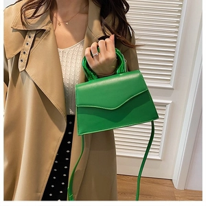 Detailed shot of green crossbody bag featuring a unique round metallic handle and stitching
