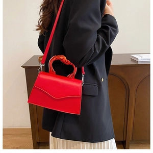 Macro view of red structured bag with unique twisted metal handle and stitching details