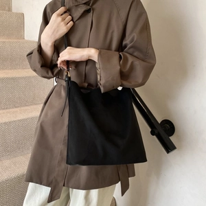 Detail of a black matte hobo bag with adjustable strap worn on a stylish trench coat