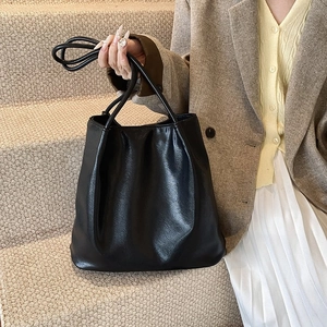 Close-up of black pleated faux leather tote bag with slim handles on stairs