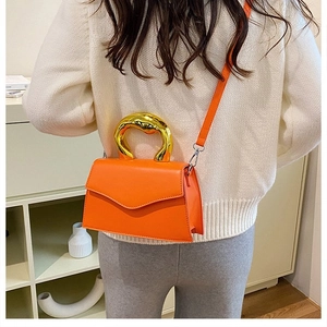 Detailed view of orange handbag featuring a unique gold molten-effect round metal handle