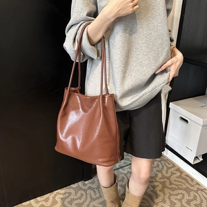 Close-up of brown leather tote bag with dual straps held by model in minimalist setting