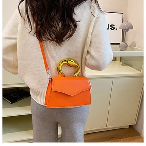 Close-up of orange crossbody bag featuring artistic gold irregular metal handle detail