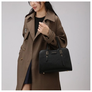 Detail of black pebbled leather handbag with gold hardware and fashion logo on trench coat
