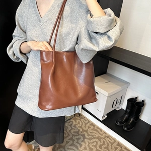 Brown leather tote bag shown on shoulder with minimalist dual straps and soft texture