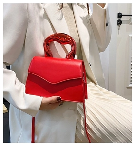Detail of a bright red shoulder bag featuring a unique wavy metallic handle and V-shaped flap