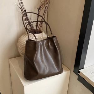 Detail of dark brown ruched leather tote bag on minimalist display stand