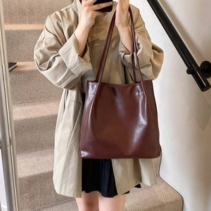 Detail of a minimalist dark brown leather tote bag worn as a chic underarm shoulder bag