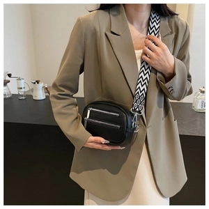 Detail of black crossbody round bag with textured leather and geometric wide strap