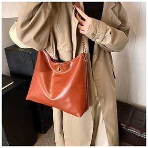 Close-up of tan leather tote bag with gold twist lock and metal chain strap on beige coat