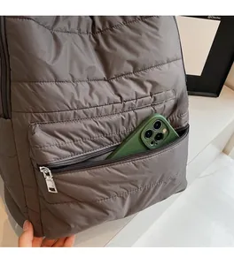 Detailed view of the front zipper pocket on a quilted nylon backpack holding a smartphone