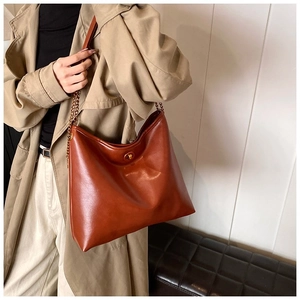 Brown leather shoulder bag with gold twist lock and chain strap on stylish beige coat