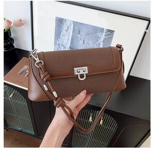 Brown leather crossbody flap bag with silver buckle and braided strap on lifestyle background