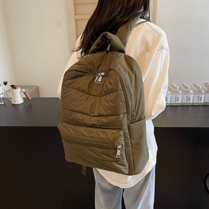 Detail showing army green quilted nylon backpack with metallic zippers on a model