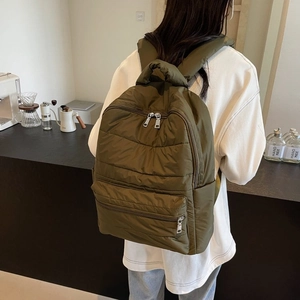 Detail of olive green quilted nylon backpack showing stitching and silver zippers