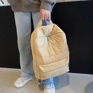 Detail of cream quilted nylon backpack showing zipper pockets and puffy seam texture
