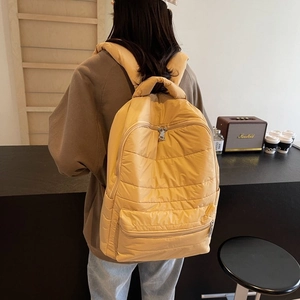 Detailed view of yellow quilted nylon backpack with horizontal stitching and wide straps