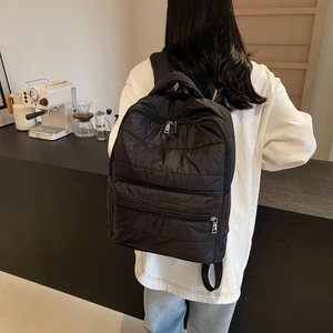 Close-up of a black quilted nylon backpack featuring silver zippers in a cafe setting