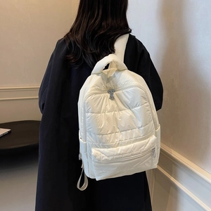 Detail of white quilted nylon backpack with padded texture and zipper pockets