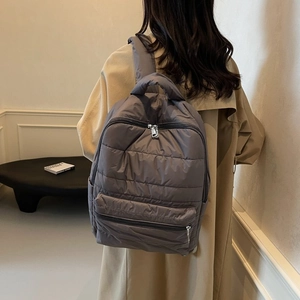 Detail of dark grey quilted nylon backpack with front zipper pocket on a model