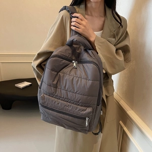 Detailed view of dark grey quilted nylon backpack with metallic silver zippers on model
