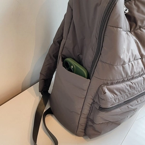 Close-up of dark grey quilted nylon backpack with side pocket holding a smartphone